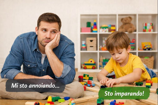 Un adulto seduto a terra appare annoiato mentre osserva un bambino concentrato che gioca con delle costruzioni su una pista. Il bambino è immerso nel gioco, l’adulto è presente ma non coinvolto.