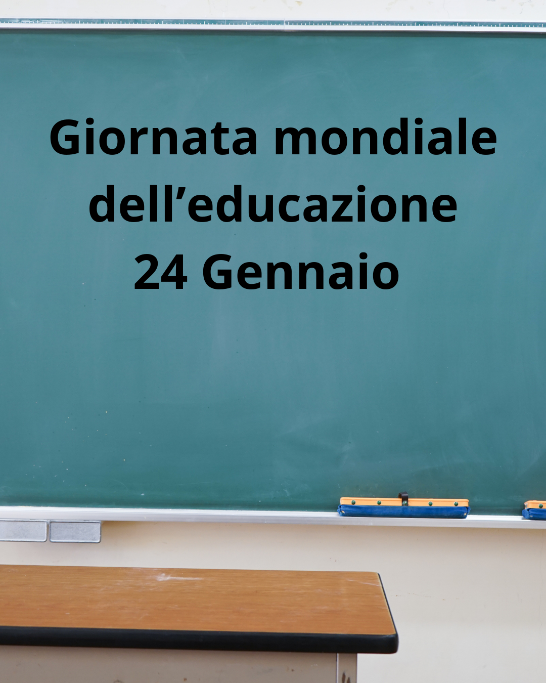Lavagna scolastica verde con la scritta in nero “Giornata mondiale dell’educazione – 24 Gennaio”. In basso si vede una cattedra e il bordo della lavagna, in un’aula vuota.